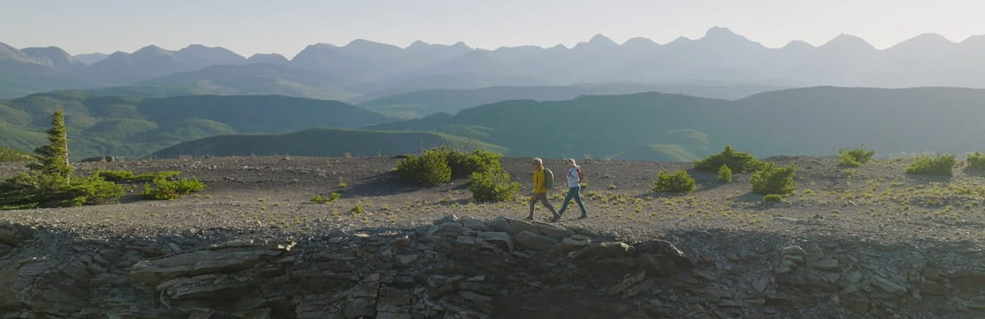 Two people walk along a mountain ridge overlooking layered peaks and open terrain, symbolizing the Medicare Annual Enrollment Period and reviewing coverage options for the year ahead.